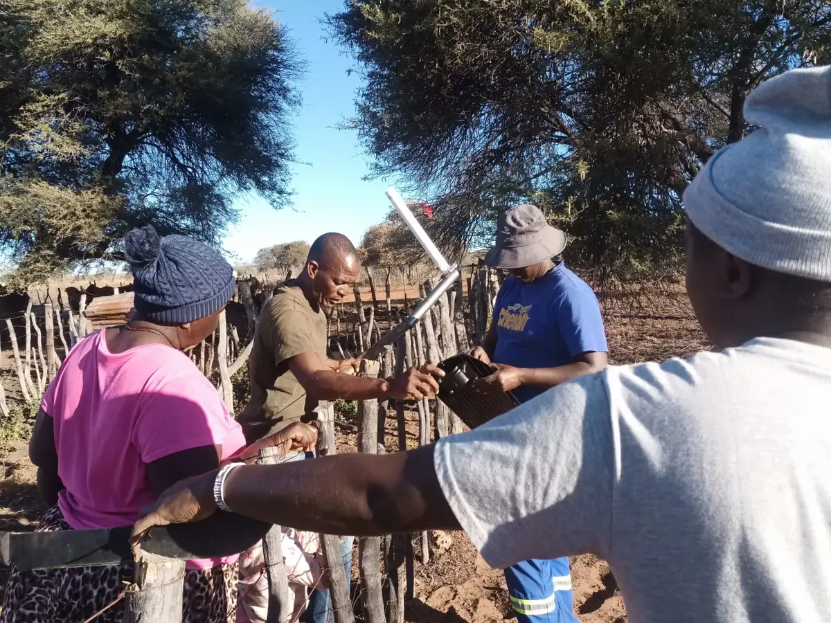 Farmers and a CCF team member fit a fox light to a wooden kraal fence