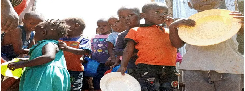Young children holding plates stand in line for a meal