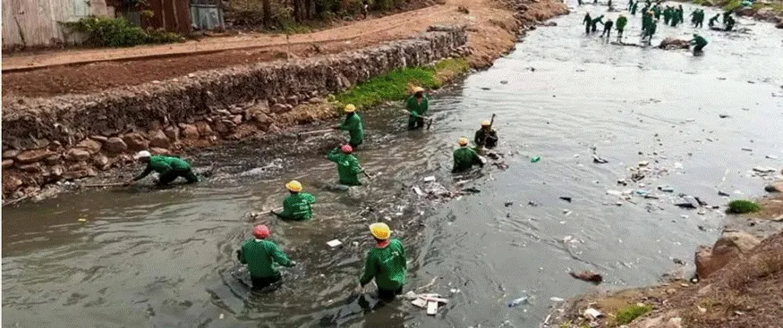 Komb Green youth in green overalls and hard hats clear rubbish from the river