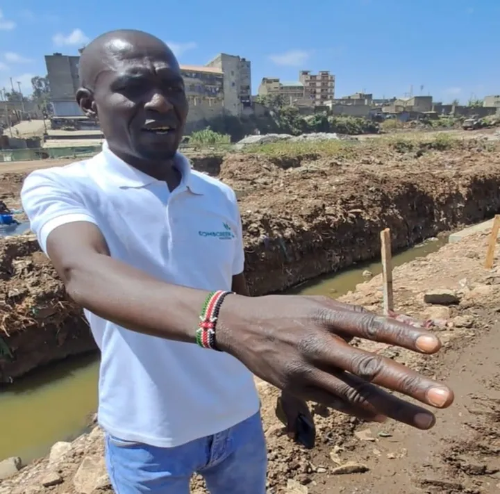An EarthTeam member in Nairobi stands beside a river channel and points to the work on the project