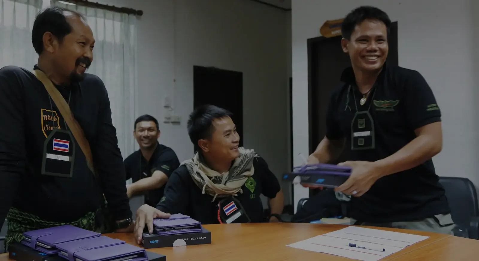 Uniformed wildlife protection officers smiling around a table as tablets are handed out at a training session